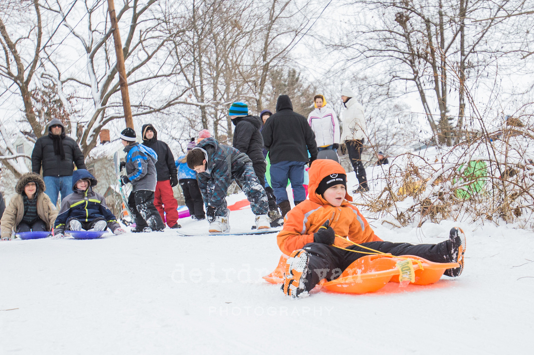 Children sledding down a hill on a snow day from school. Photo by Deirdre Ryan Photography