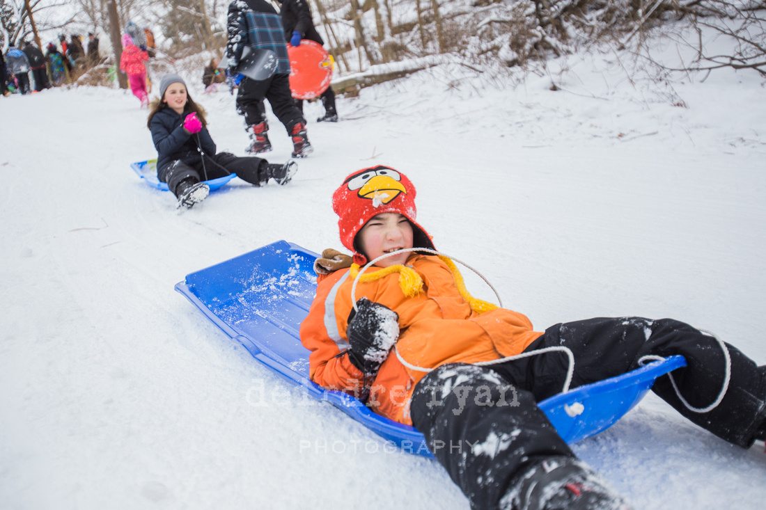 Children sledding down a hill on a snow day from school. Photo by Deirdre Ryan Photography